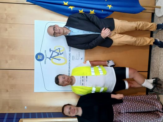 Image from left to right shows Claire Depre, Head of Unit Road Safety, DG MOVE, cyclist Adam Sobiera and Torsten Klimke, Head of Unit Innovation and Research, DG MOVE. They are all standing in front the European Declaration on Cycling poster on the wall.