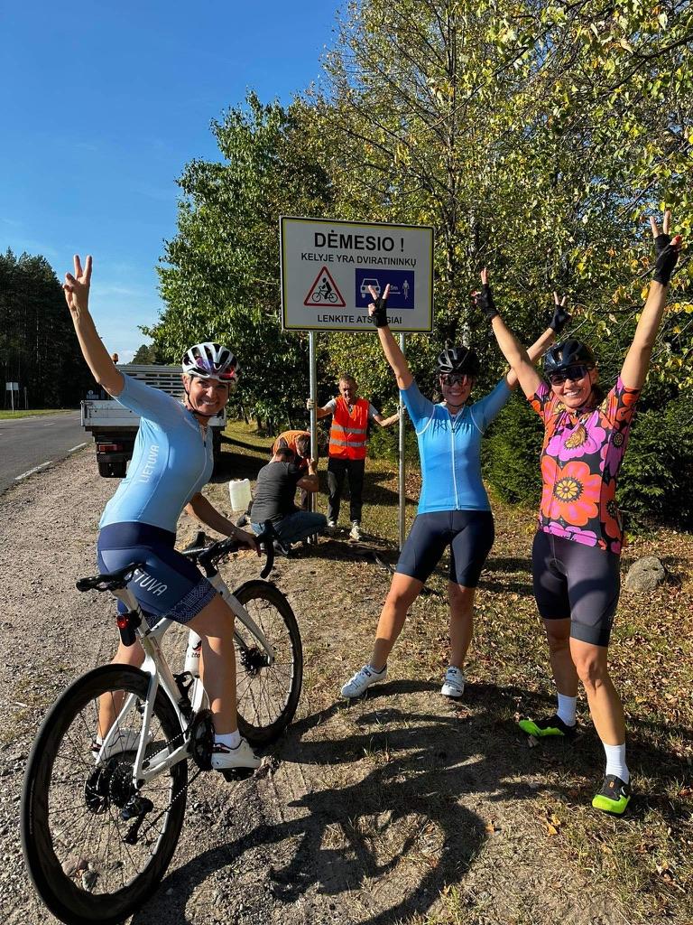 Three cyclist women with hands in the air celebrating 1.5 meter sign installation